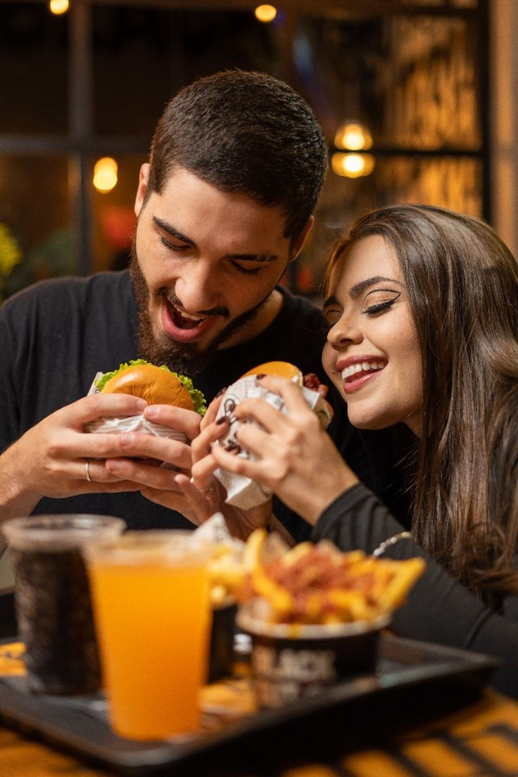 Casal sorrindo com hambúrgueres e batatas fritas sobre a mesa