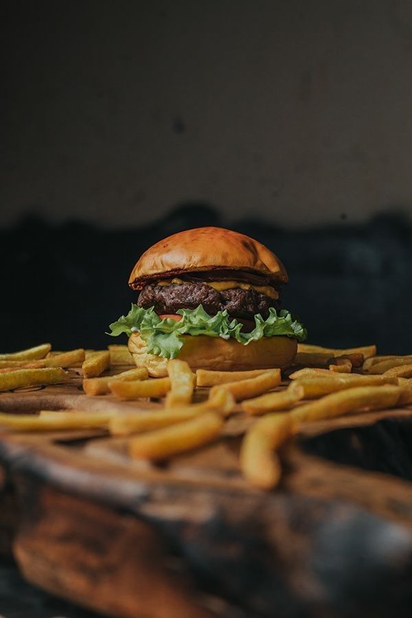 Hambúrguer com queijo derretido e batatas fritas sobre uma tábua de madeira